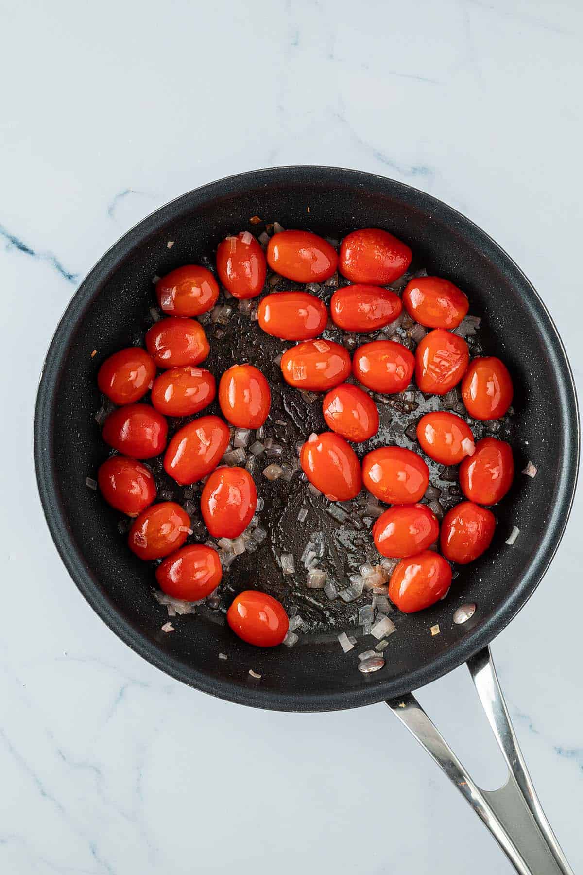 Angebratene Kirschtomaten und Schalottenw&uuml;rfel in einer Pfanne.