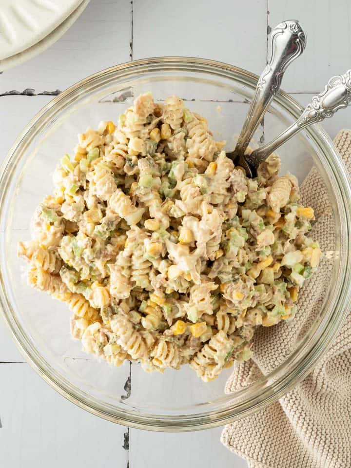 Ein cremiger Nudelsalat mit Thunfisch, Mais und Gem&uuml;se in einer gro&szlig;en Sch&uuml;ssel, Teller und ein Tuch im Bildrand.
