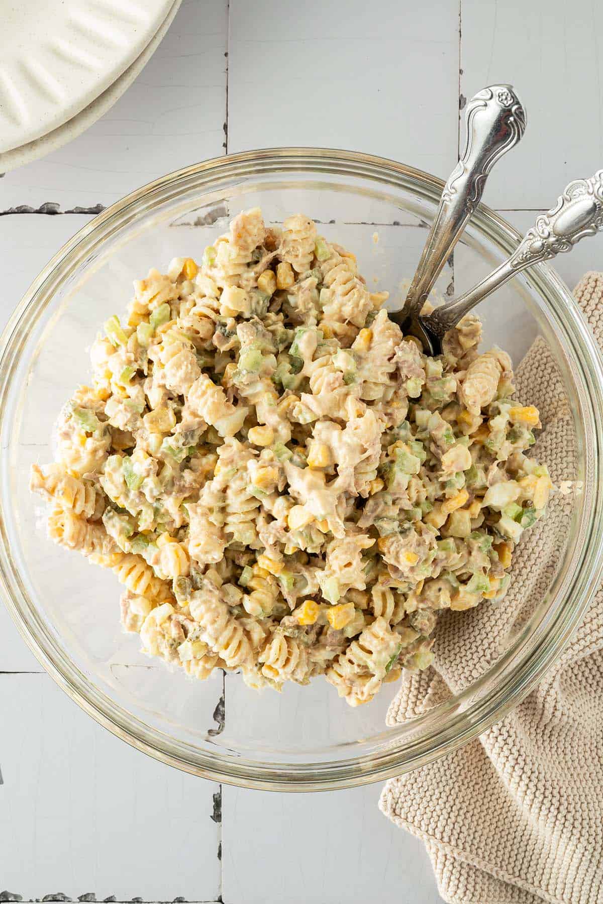 Ein cremiger Nudelsalat mit Thunfisch, Mais und Gem&uuml;se in einer gro&szlig;en Sch&uuml;ssel, Teller und ein Tuch im Bildrand.