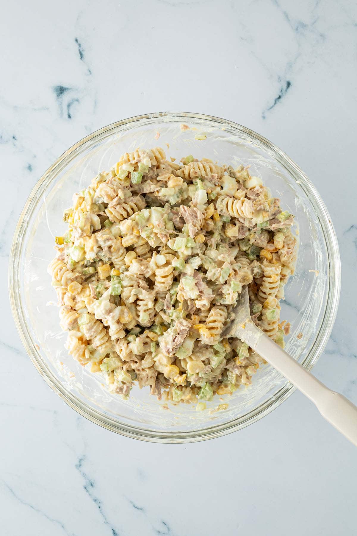 Nudelsalat wird mit Thunfisch, Mais, Gemüse und dem cremigen Dressing verrührt.