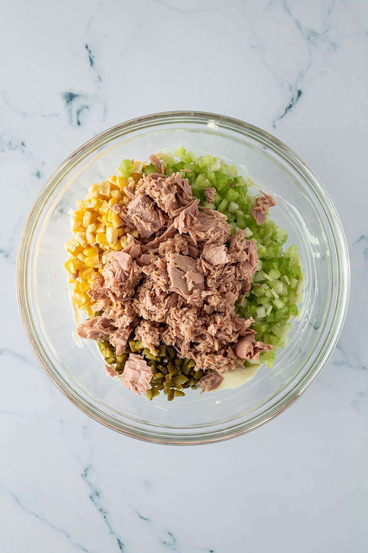 Klein gewürfelter Sellerie, Essiggurken, Thunfisch aus der Dose, Maiskörner und das cremiges Dressing in einer Schüssel.