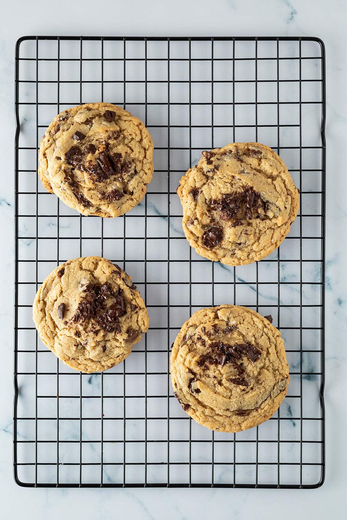 Vier frisch gebackene Chocolate Chip Cookies mit groben Schokost&uuml;cken auf einem schwarzen Kuchengitter.