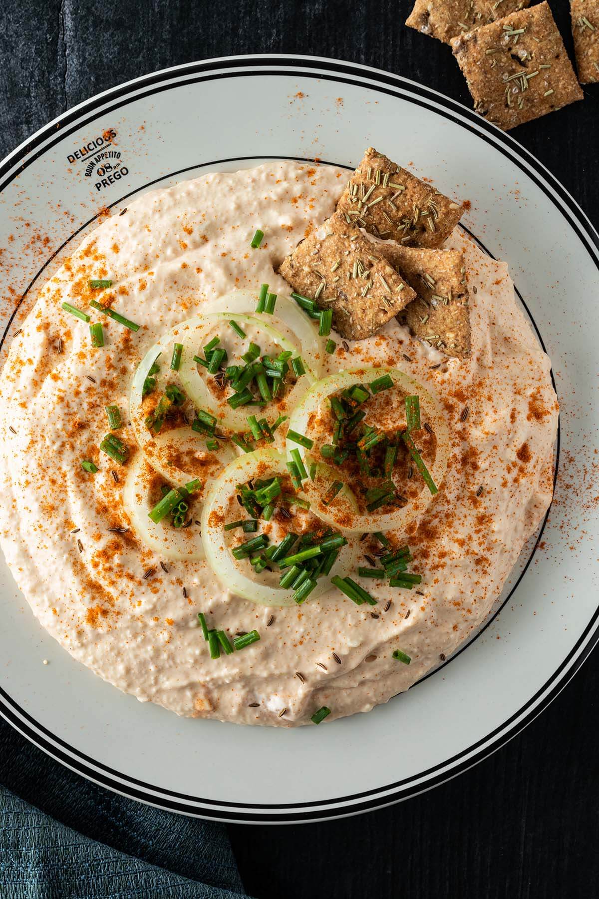 Cremiger Obazda mit Zwiebelringen und frischem Schnittlauch, serviert mit Crackern.