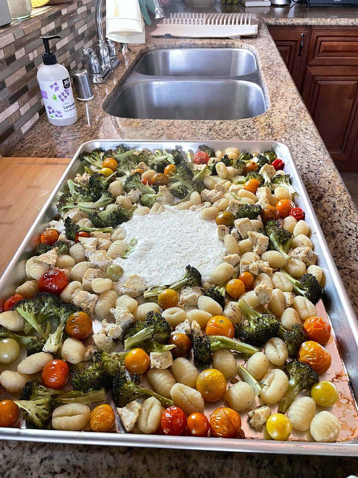 K&uuml;chenarbeitsfl&auml;che mit einem Blech mit Gem&uuml;se, Gnocchi und H&uuml;ttenk&auml;se in der Mitte.