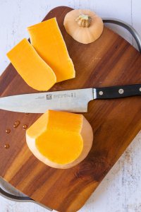 Von einem Butternutk&uuml;rbis wird mit einem Messer die Schale abgeschnitten.