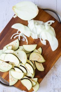 In Halbmond-Form geschnittene Aubergine und Zwiebelringe auf einem Holzbrett.