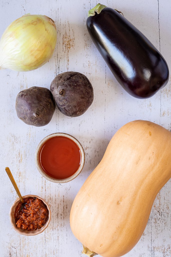 Das Bild zeigt einen Butternutk&uuml;rbis, eine Aubergine, eine gro&szlig;e, wei&szlig;e Zwiebel, zwei Rote Bete Knollen, passierte Tomaten und rote Pesto.