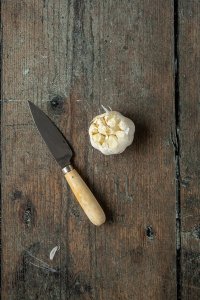 Eine Knoblauchknolle, deren Kopf abgeschnitten ist, daneben ein K&uuml;chenmesser.