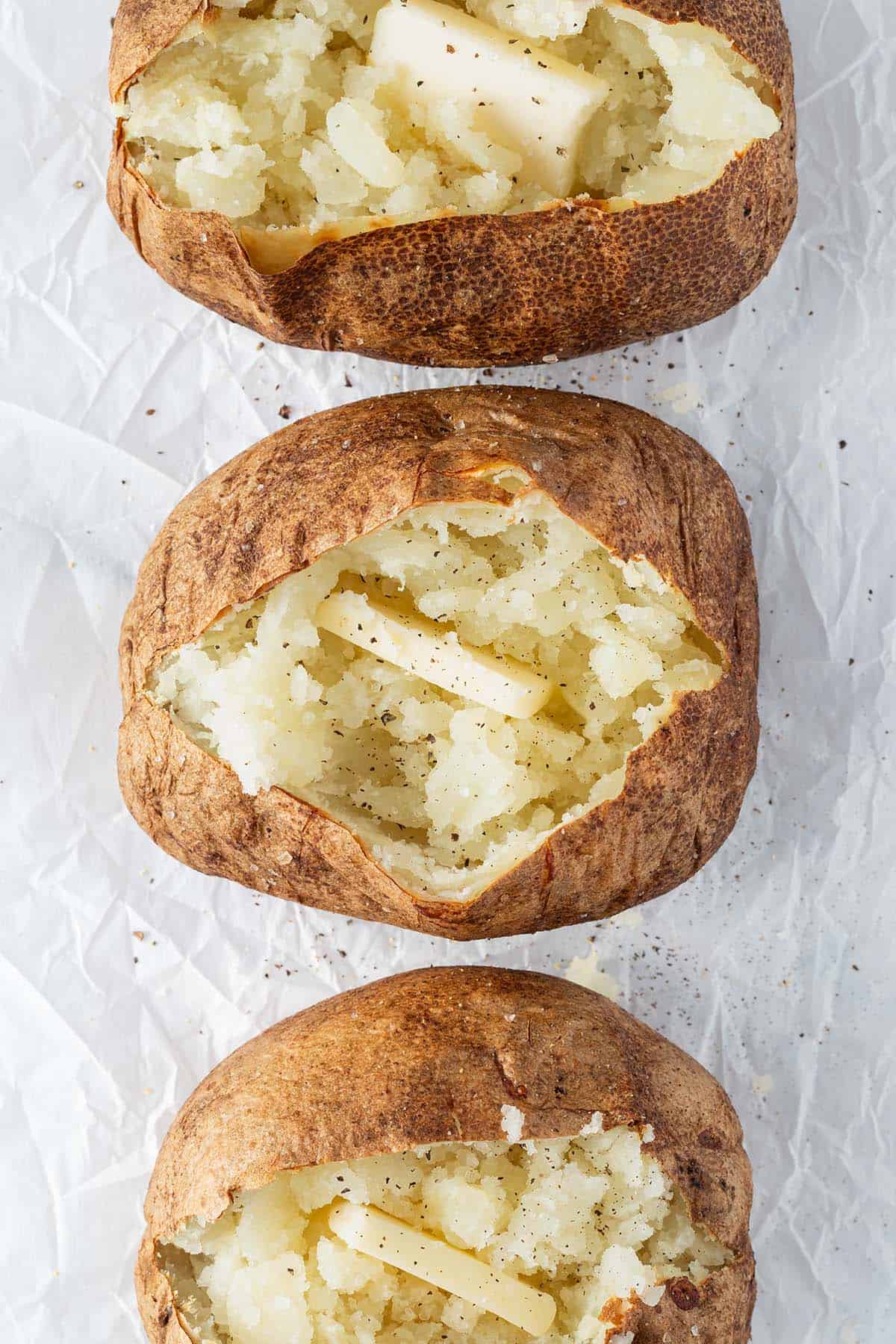 Drei aufgeschnittene Ofenkartoffeln mit einem St&uuml;ckchen Butter.