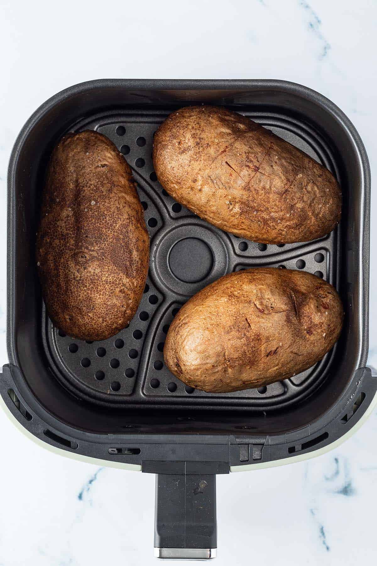 Drei gebackene Kartoffeln in einer Hei&szlig;luftfritteuse.