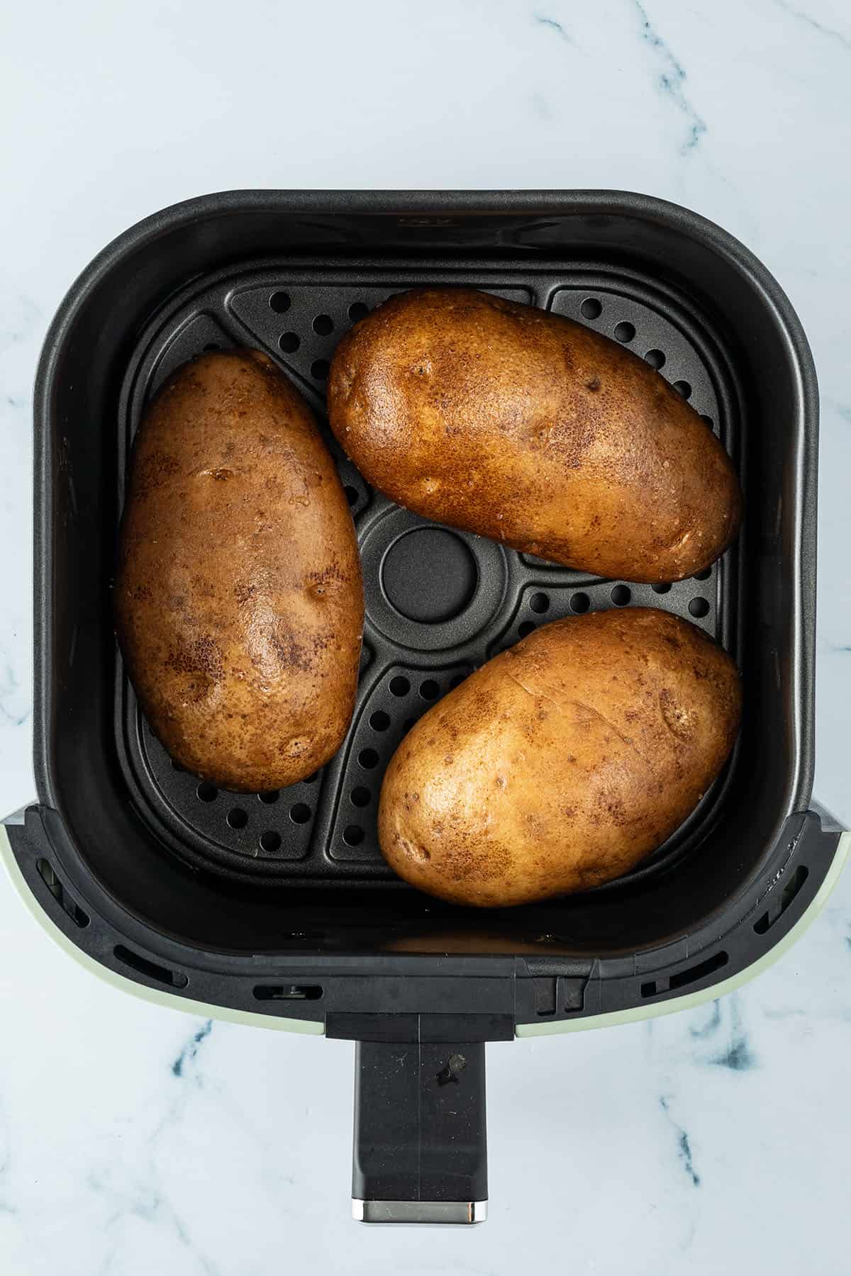 Drei gro&szlig;e, rohe Kartoffeln in einem Airfryer Korb.