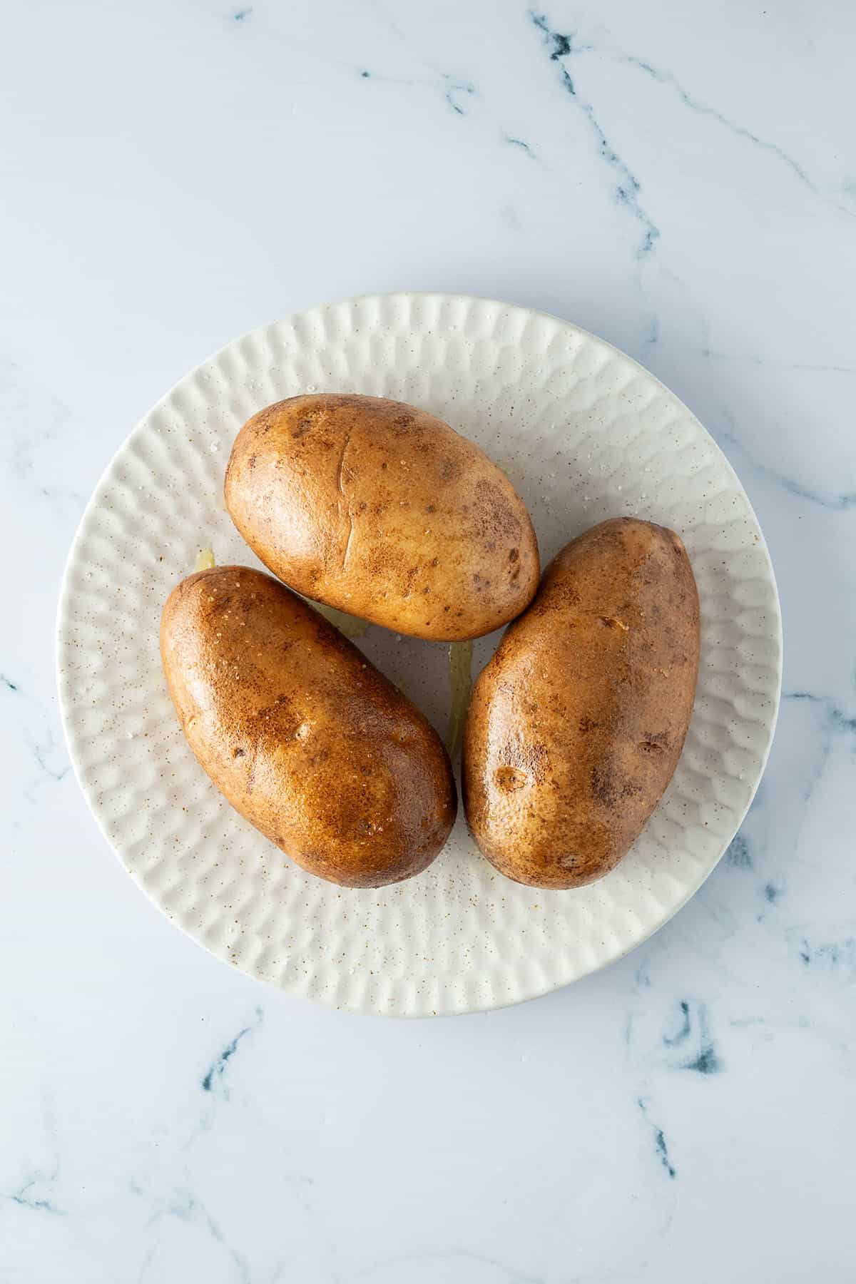 Drei gro&szlig;e Kartoffeln, deren Schale mit &Ouml;l und Salz eingerieben wurde, auf einem Teller.