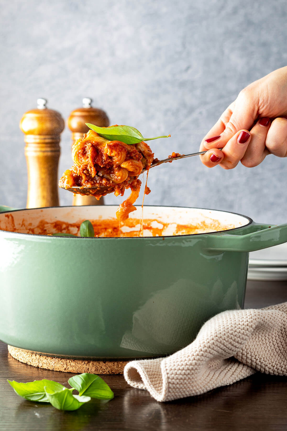 Eine Hand nimmt ein L&ouml;ffel Nudeln in einer Hackfleisch-Tomaten-Sauce aus einem Topf.