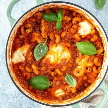 Vogelperspektive auf einen Topf mit einer One Pot Lasagne mit geschmolzenem Mozzarella und frischem Basilikum, Deko im Bildrand.