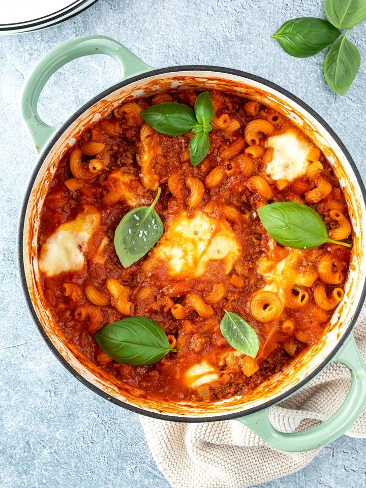 Vogelperspektive auf einen Topf mit einer One Pot Lasagne mit geschmolzenem Mozzarella und frischem Basilikum, Deko im Bildrand.