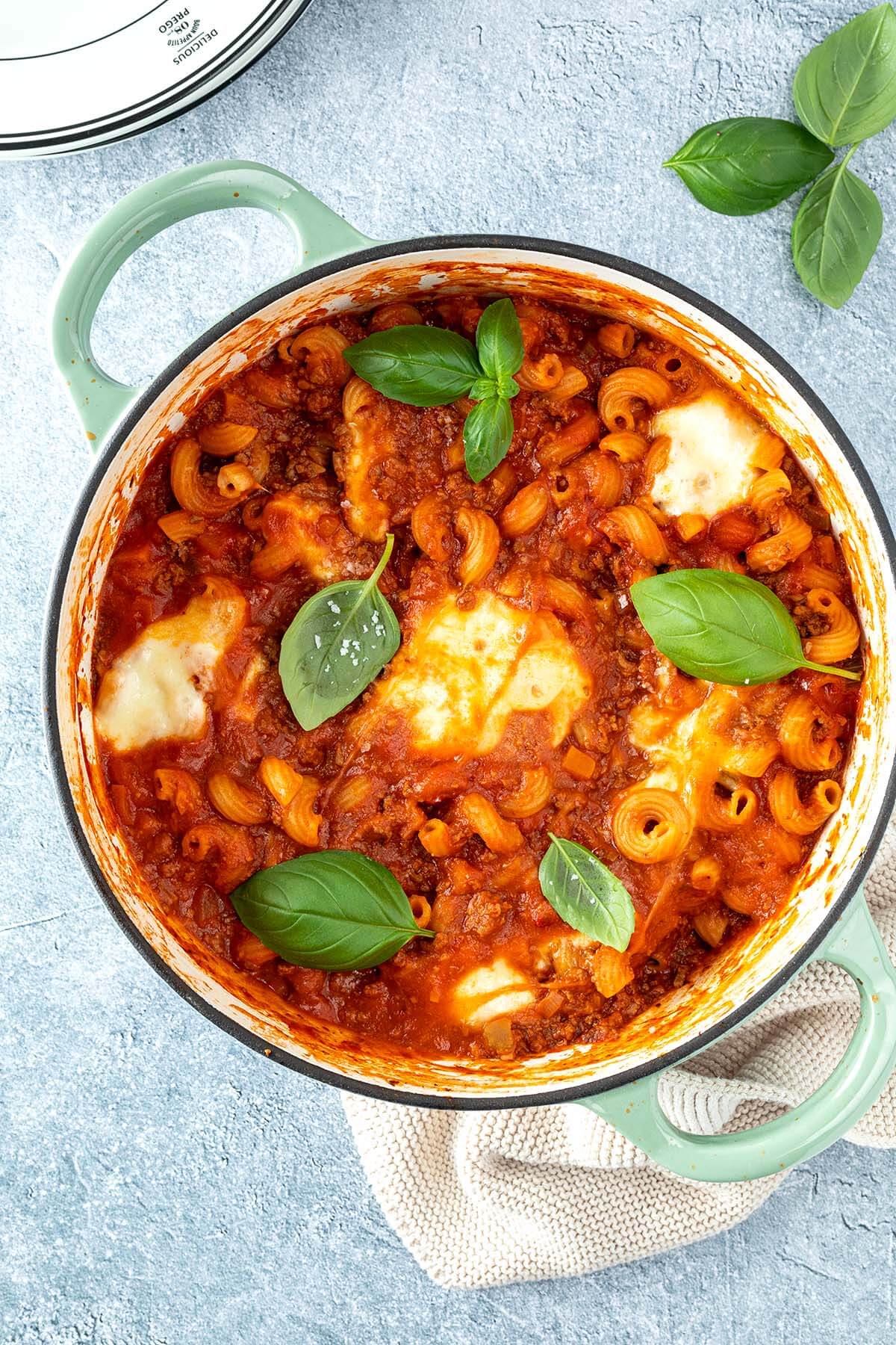 Vogelperspektive auf einen Topf mit einer One Pot Lasagne mit geschmolzenem Mozzarella und frischem Basilikum, Deko im Bildrand.