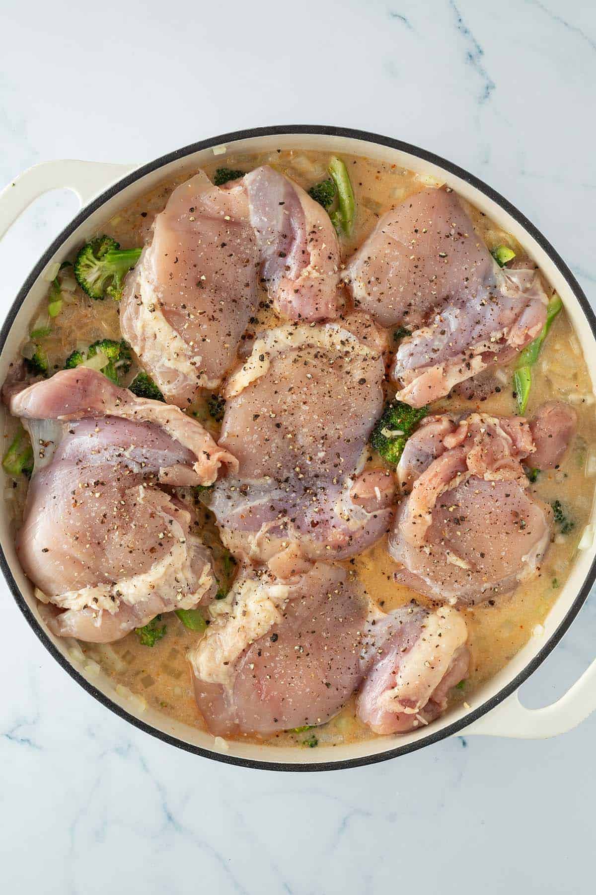 Reis, Brokkoli und Sauce in einer Pfanne mit rohen H&auml;hnchenst&uuml;cken on top.
