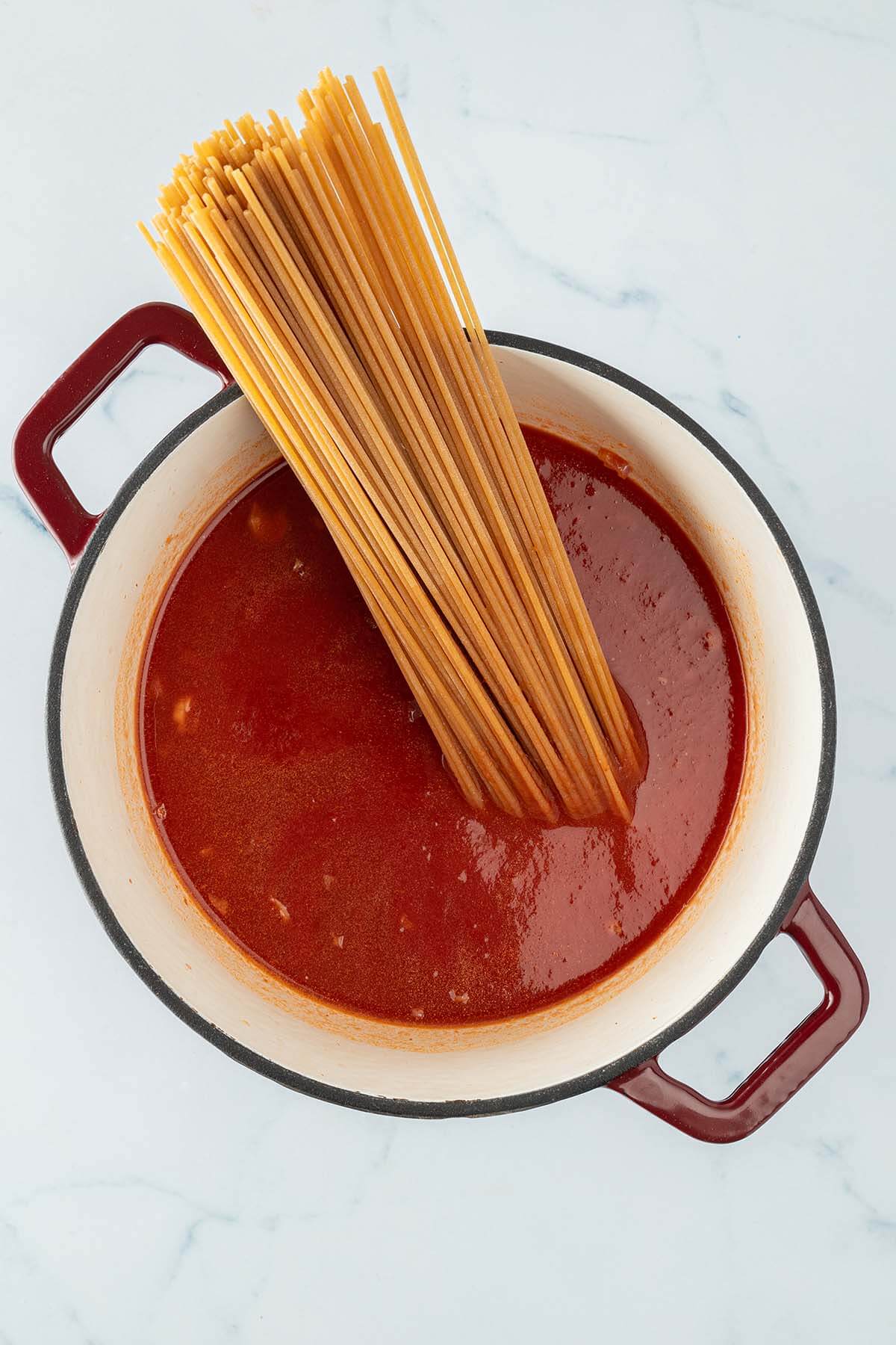Topf mit Tomatensauce, in der ungekochte Spaghetti senkrecht drin stehen.