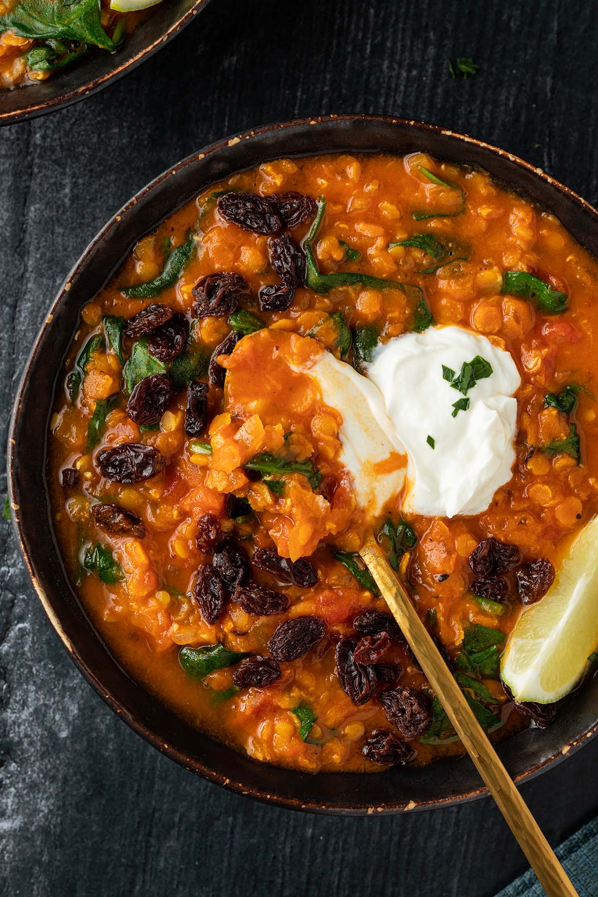 Nahaufnahme von einer Sch&uuml;ssel mit einer orientalischen, roten Linsensuppe, die mit Joghurt, Rosinen, Limette und frischen Kr&auml;utern serviert wird.