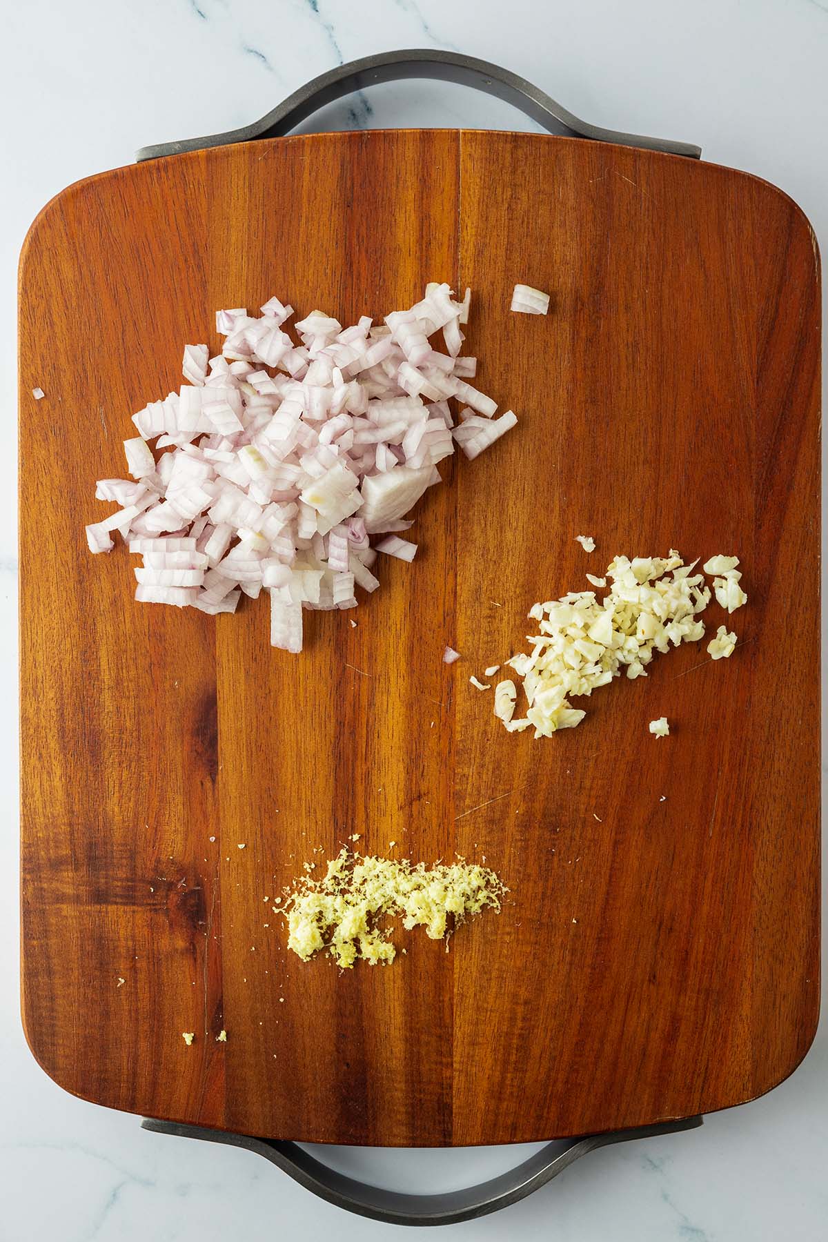 Kleingew&uuml;rfelte Zwiebeln und Knoblauchst&uuml;cke sowie geriebener Ingwer auf einem Holzbrett.