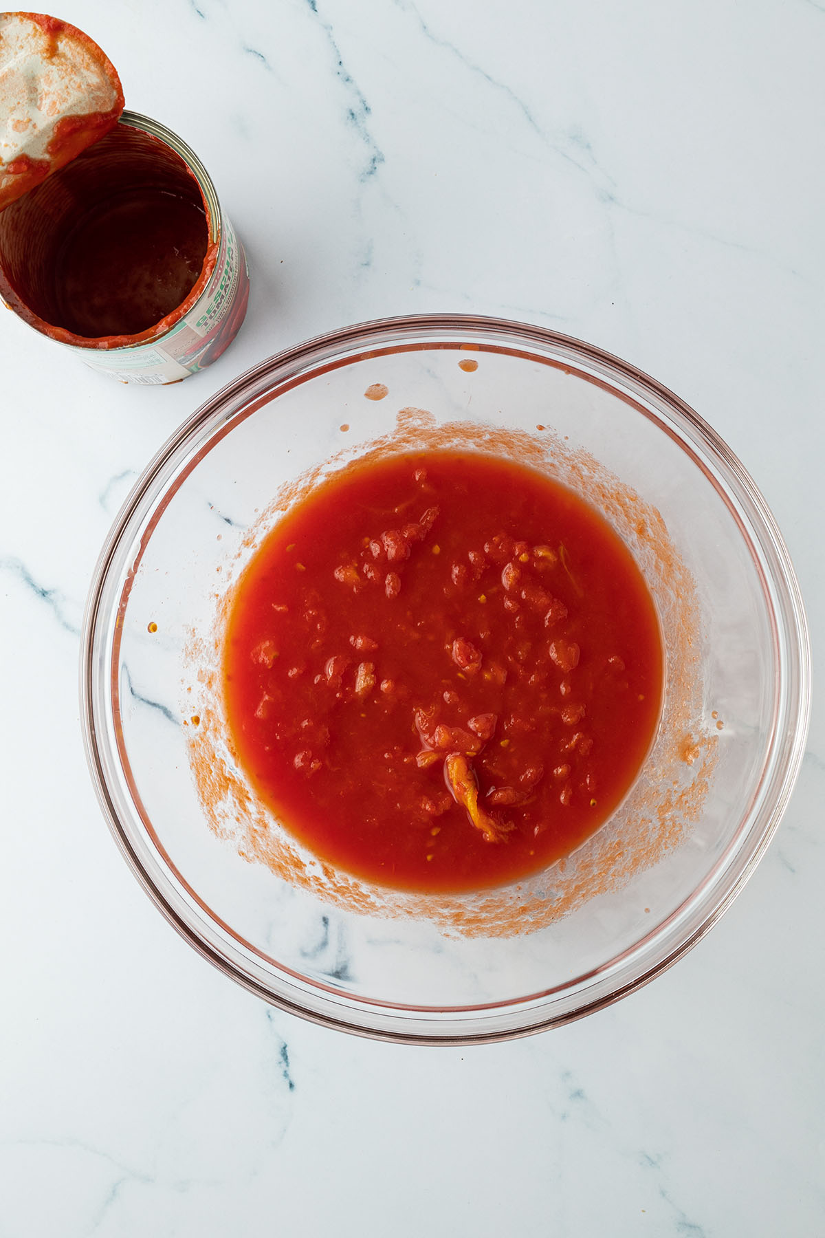 Eine Dose gesch&auml;lte und per Hand zerdr&uuml;ckte Tomaten in einer Glassch&uuml;ssel.