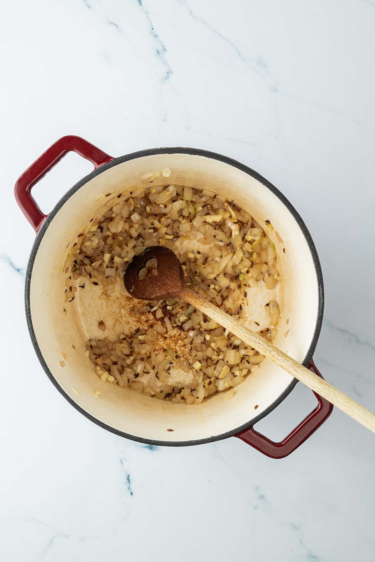 Glasig angebratene Zwiebel- und Knoblauchw&uuml;rfel mit Gew&uuml;rzen in einem Topf.