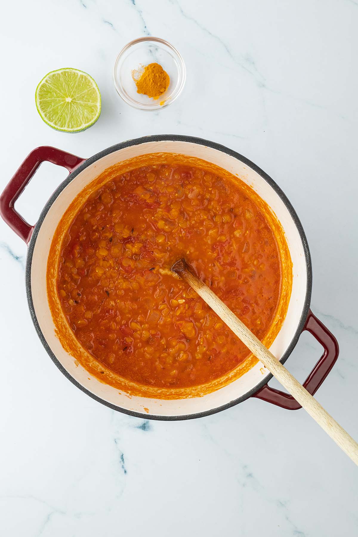 Stickige rote Linsensuppe in einem Topf, daneben eine halbe Limette und ein Sch&auml;lchen Kurkuma.