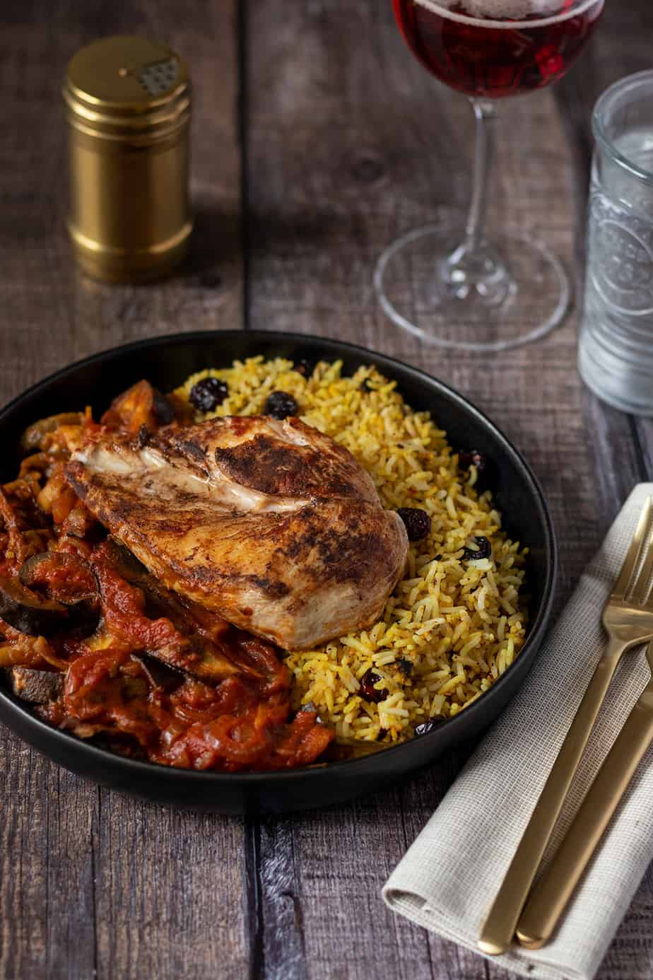 Orientalisches H&auml;hnchen serviert mit Auberginen-Tomatensauce und Curryreis, Deko im Hintergrund.