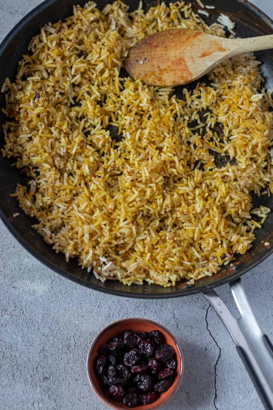 Curryreis in einer Pfanne mit einer Schüssel Cranberries daneben.