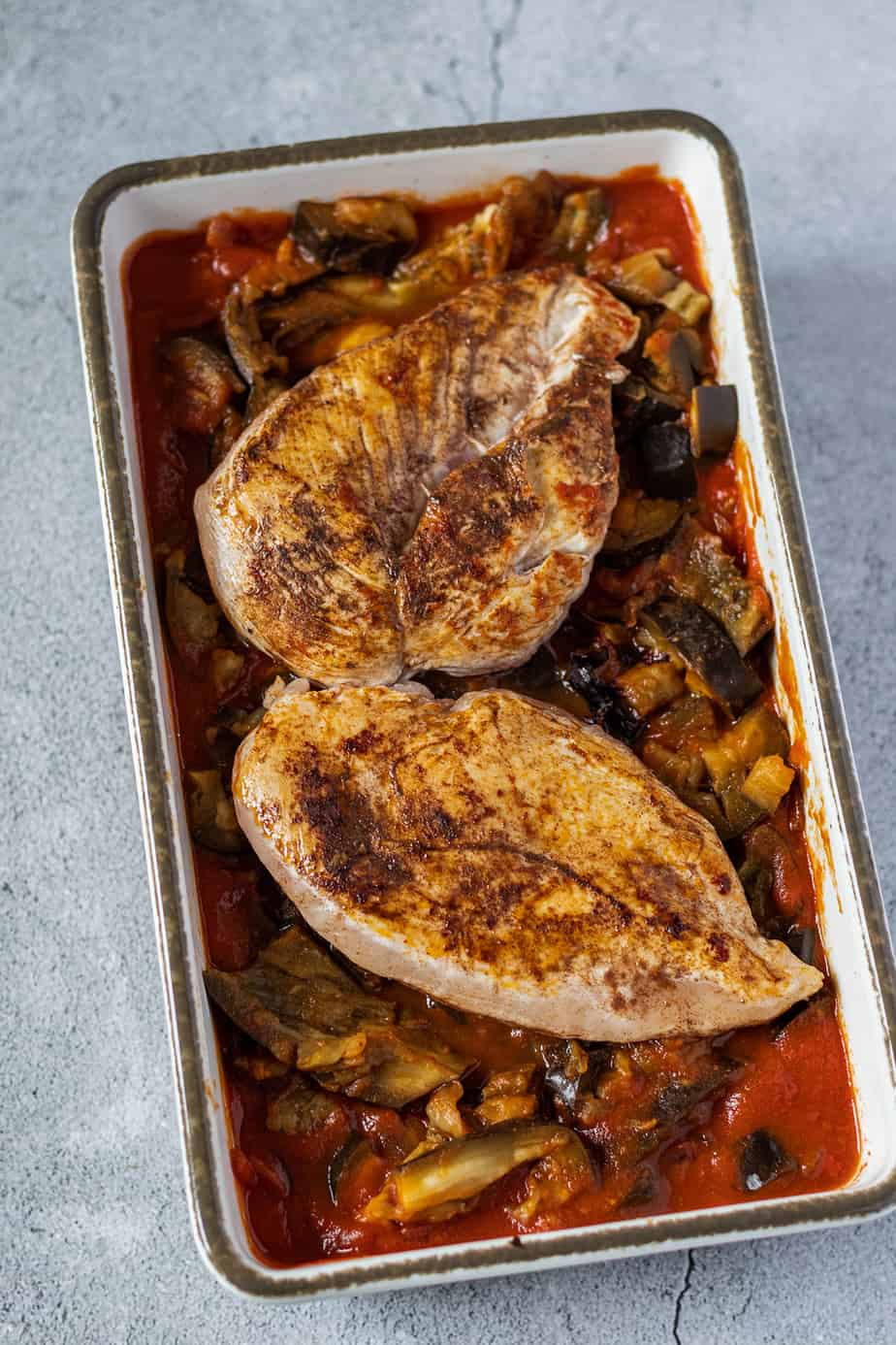 Kurz angebratene Hähnchenfilets in einer Auflaufform auf einer Tomaten-Auberginensoße.