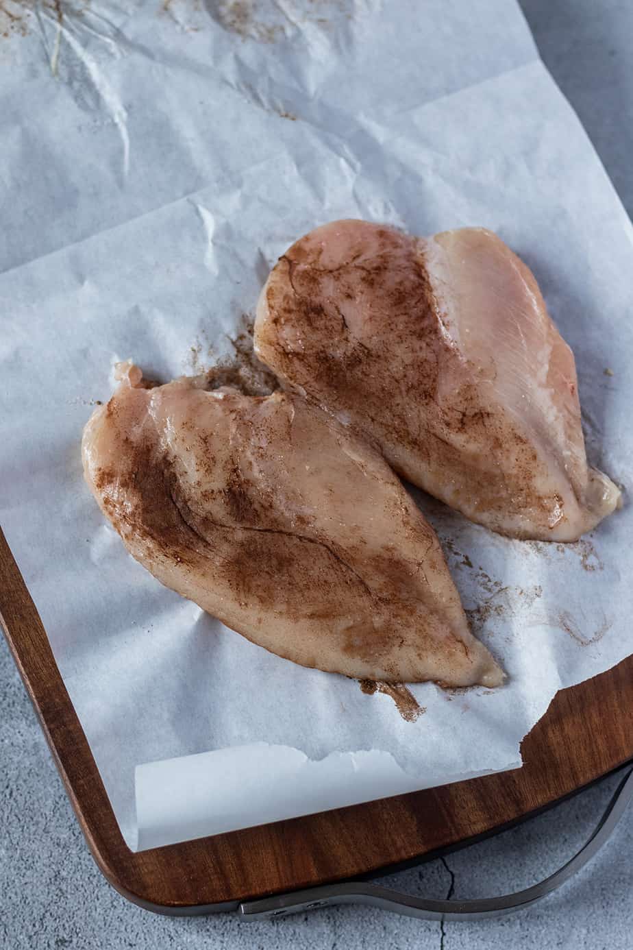 Zwei gewürzte und dünner geklopfte Hähnchenfilets auf Butterbrotpapier.