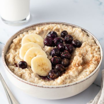 Eine Sch&uuml;ssel mit traditionellem Porridge aus Hafergr&uuml;tze mit Blaubeeren und Banane on top und einem Glas Milch im Hintergrund.