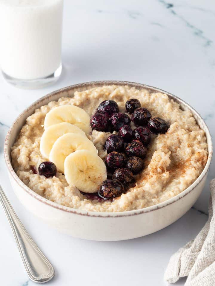 Eine Sch&uuml;ssel mit traditionellem Porridge aus Hafergr&uuml;tze mit Blaubeeren und Banane on top und einem Glas Milch im Hintergrund.