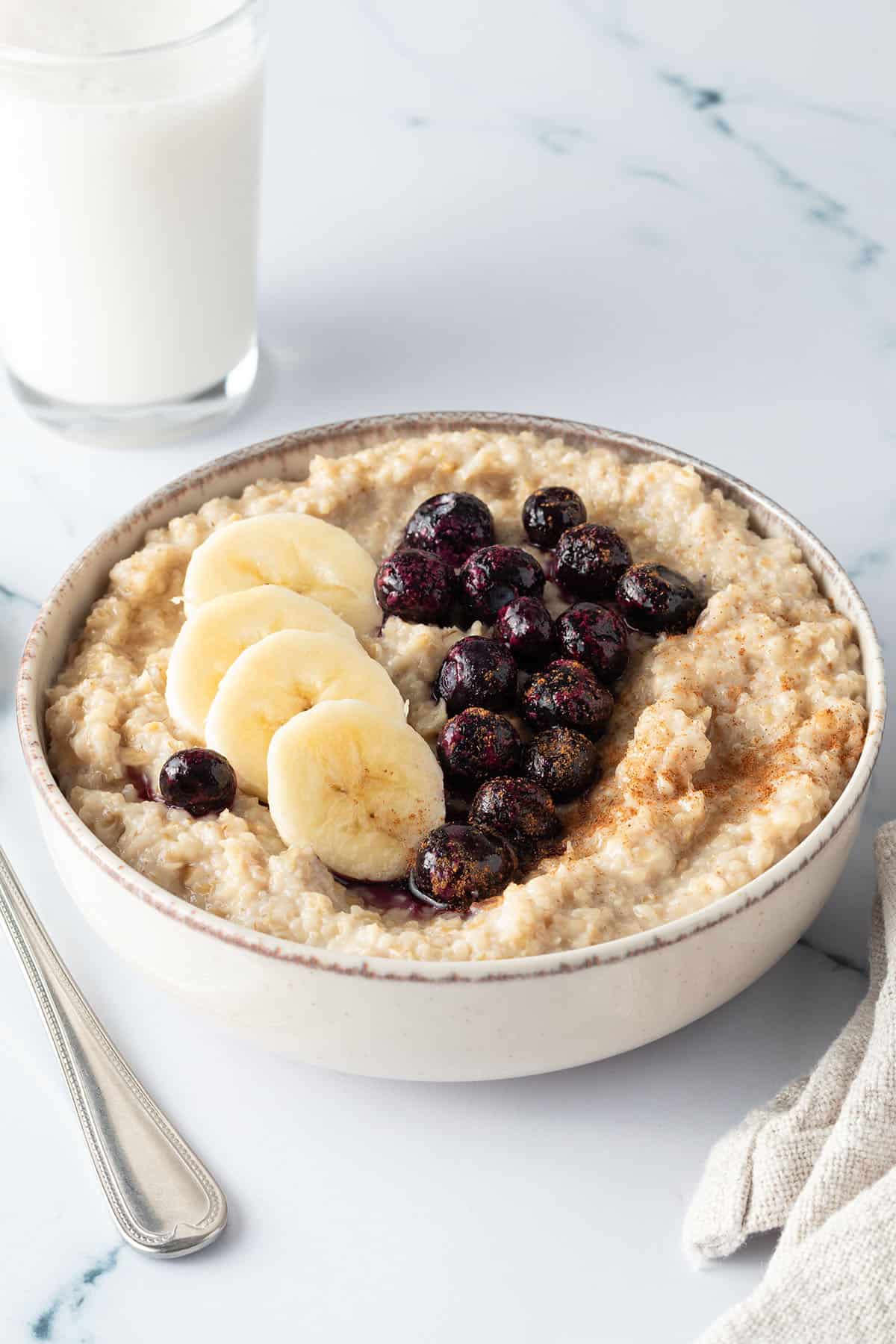 Eine Sch&uuml;ssel mit traditionellem Porridge aus Hafergr&uuml;tze mit Blaubeeren und Banane on top und einem Glas Milch im Hintergrund.
