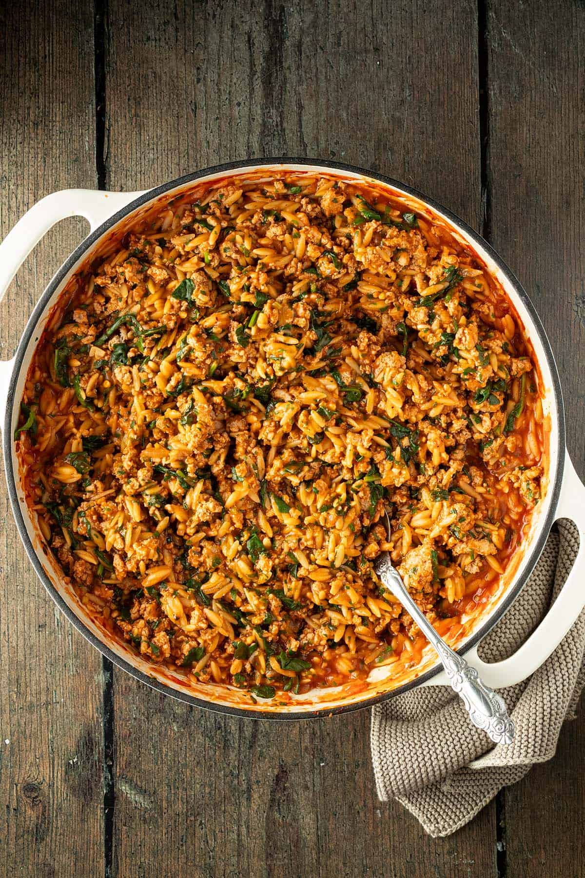 Orzo Pfanne mit Hackfleisch und Spinat auf einem dunklen Holzuntergrund.