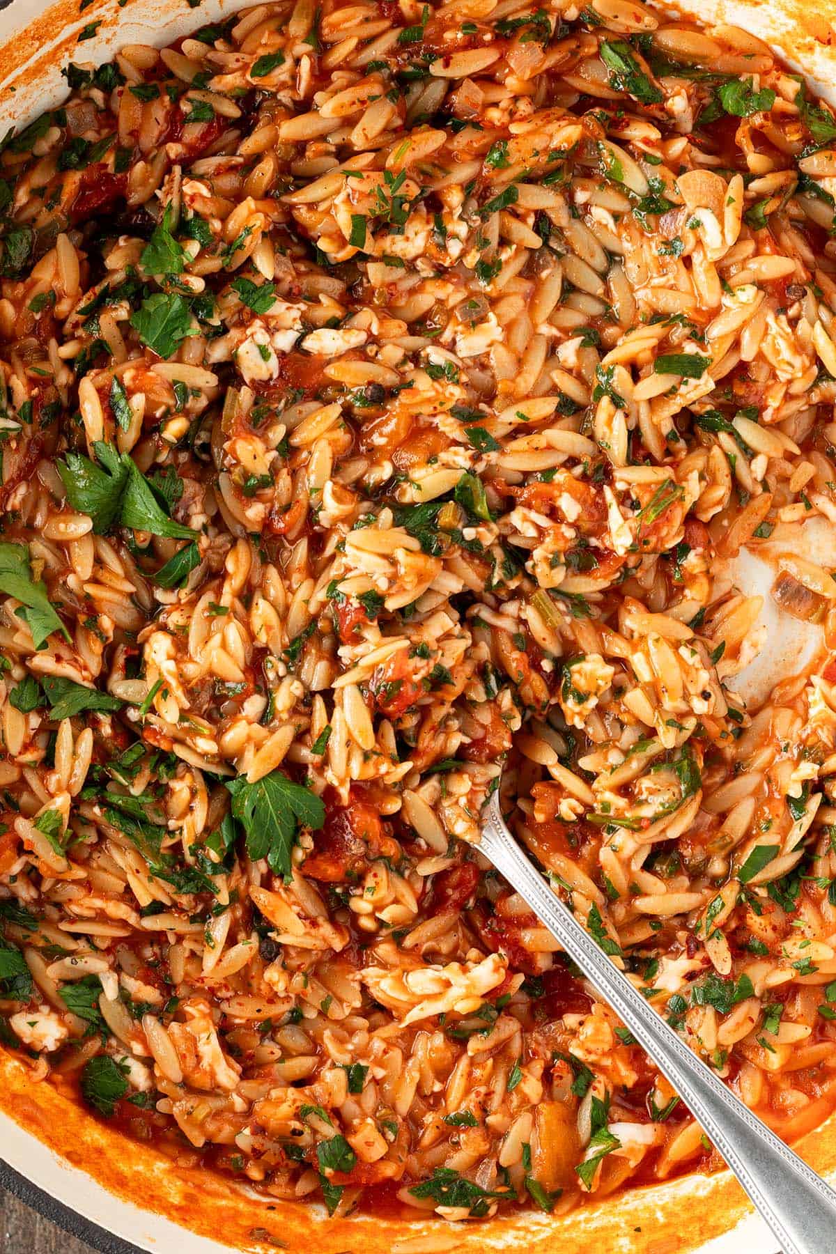 Cremiges Orzo Risotto mit geriebenem Halloumi, Tomate und Petersilie in einer Pfanne.