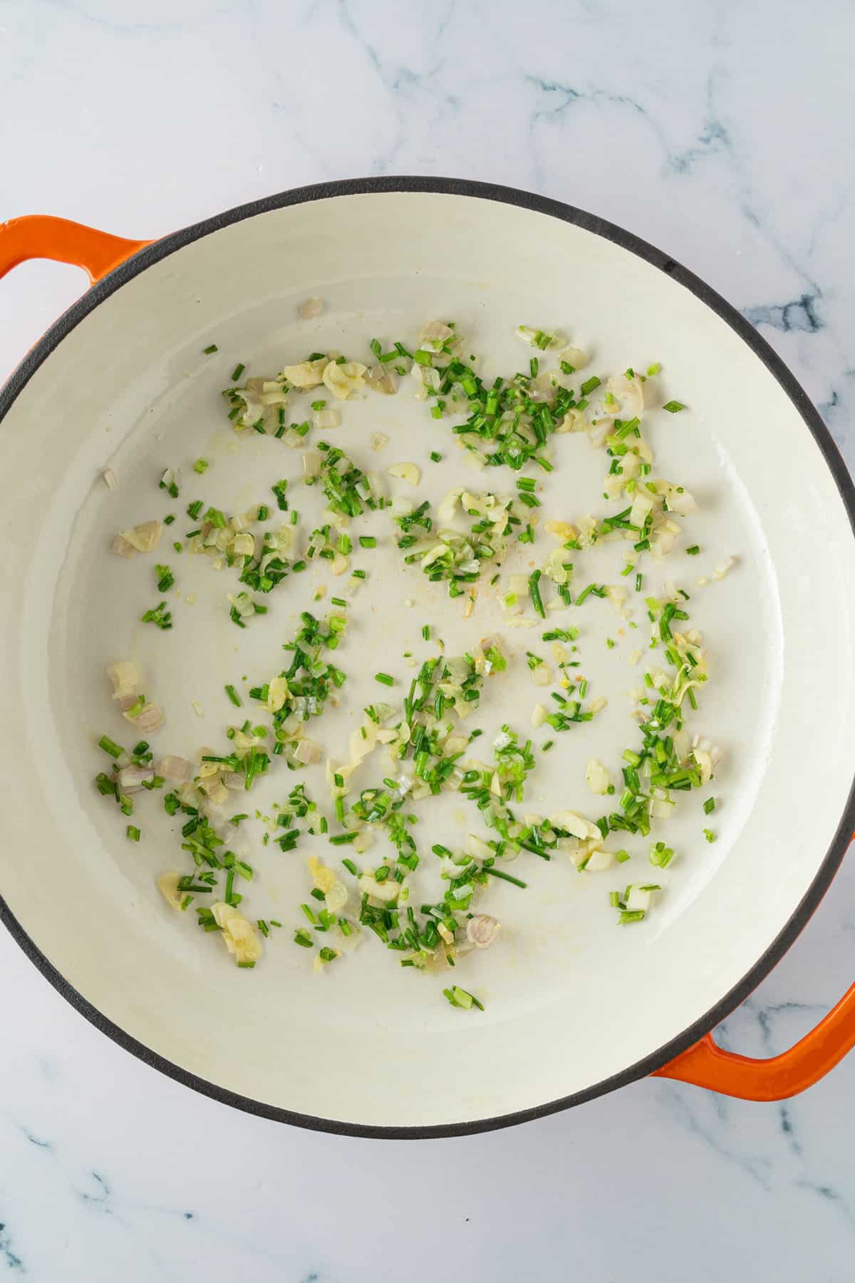 Fein gehackter Knoblauch, Schalotte und Petersilienst&auml;ngel werden in einer tiefen Pfanne mit &Ouml;l anged&uuml;nstet.