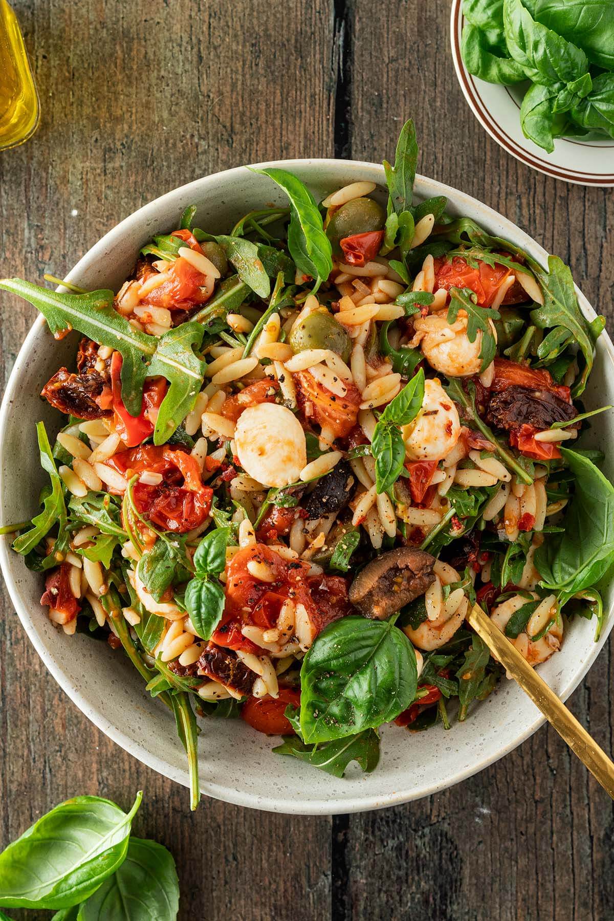 Vogelperspektive auf einen Teller mit einem Kritharaki-Nudelsalat mit Tomaten, Oliven, Mozzarella, Rucola und Tomaten.