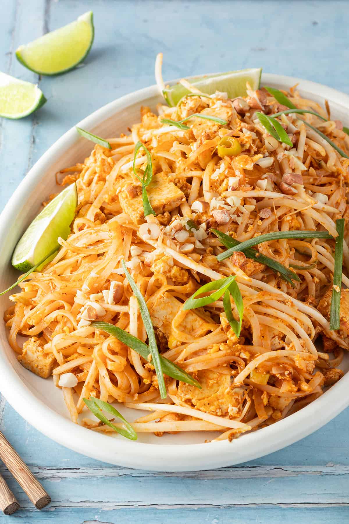 Pad Thai mit Tofu serviert auf einem gro&szlig;en Teller mit Fr&uuml;hlingszwiebeln und Limetten.