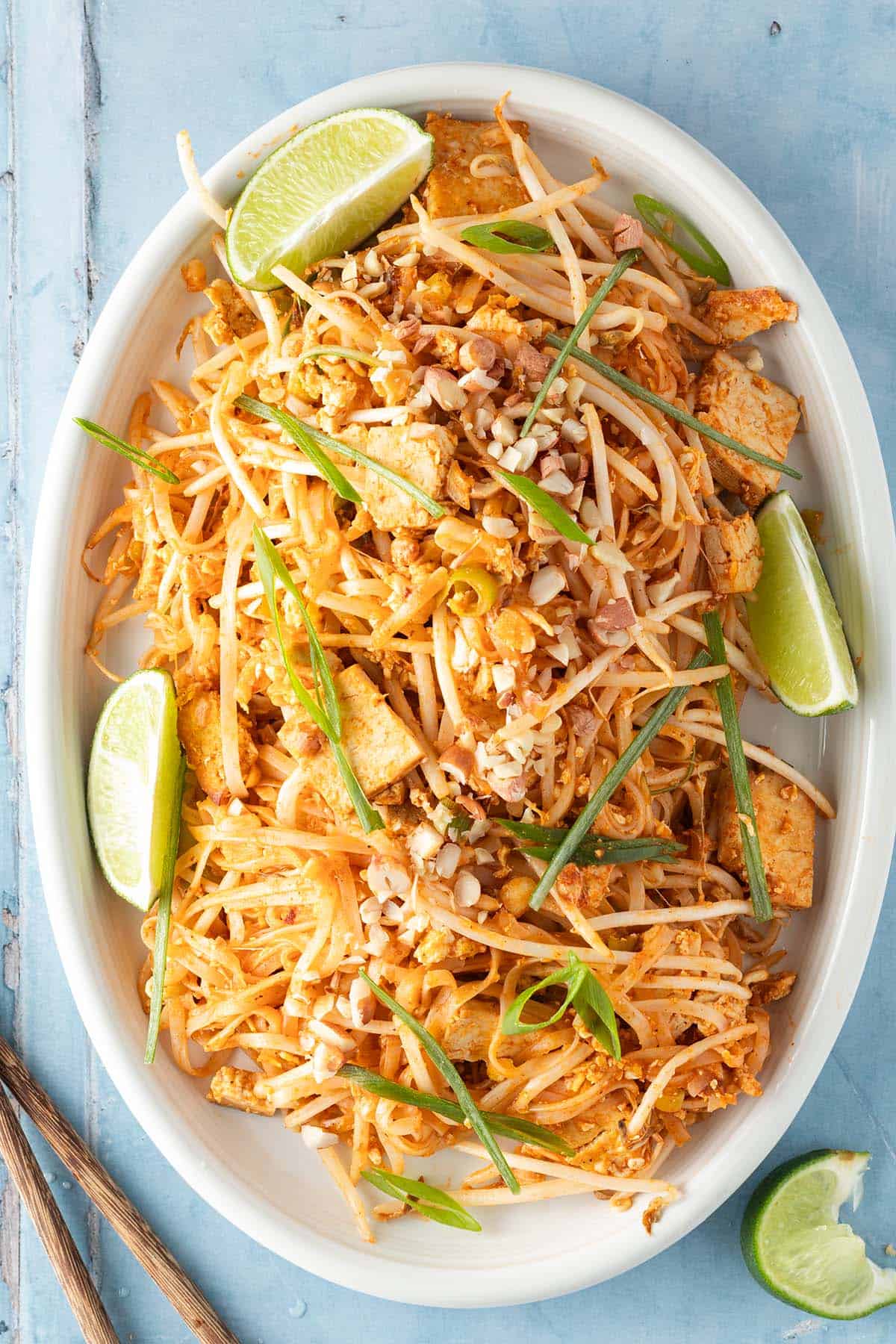 Ein gro&szlig;er Teller mit vegetarischem Tofu Pad Thai mit Limettenspalten und Fr&uuml;hlingszwiebeln.