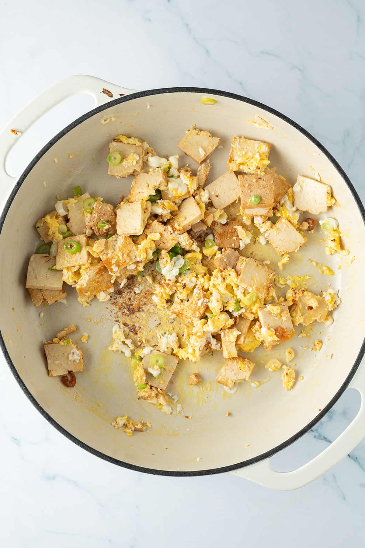 Gestocktes R&uuml;hrei in einer Pfanne mit Tofu, Knoblauch und Fr&uuml;hlingszwiebeln.