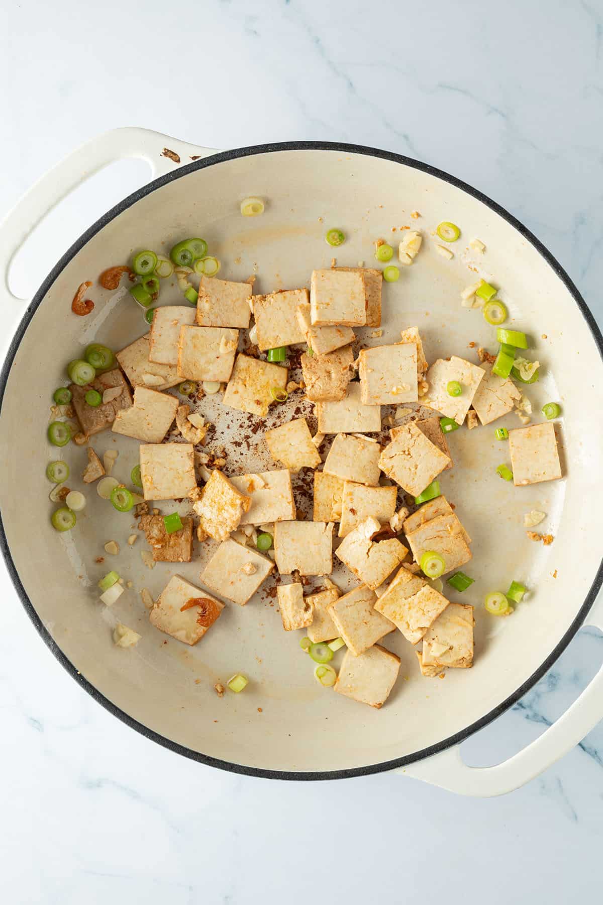 Knoblauch und Fr&uuml;hlingszwiebeln werden mit dem Tofu in der Pfanne angebraten.