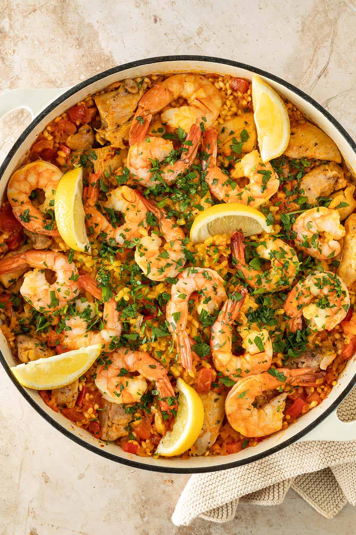 Paella mit H&auml;hnchen und Garnelen, garniert mit frischer Petersilie und Zitronenspalten, in einer gro&szlig;en Pfanne.