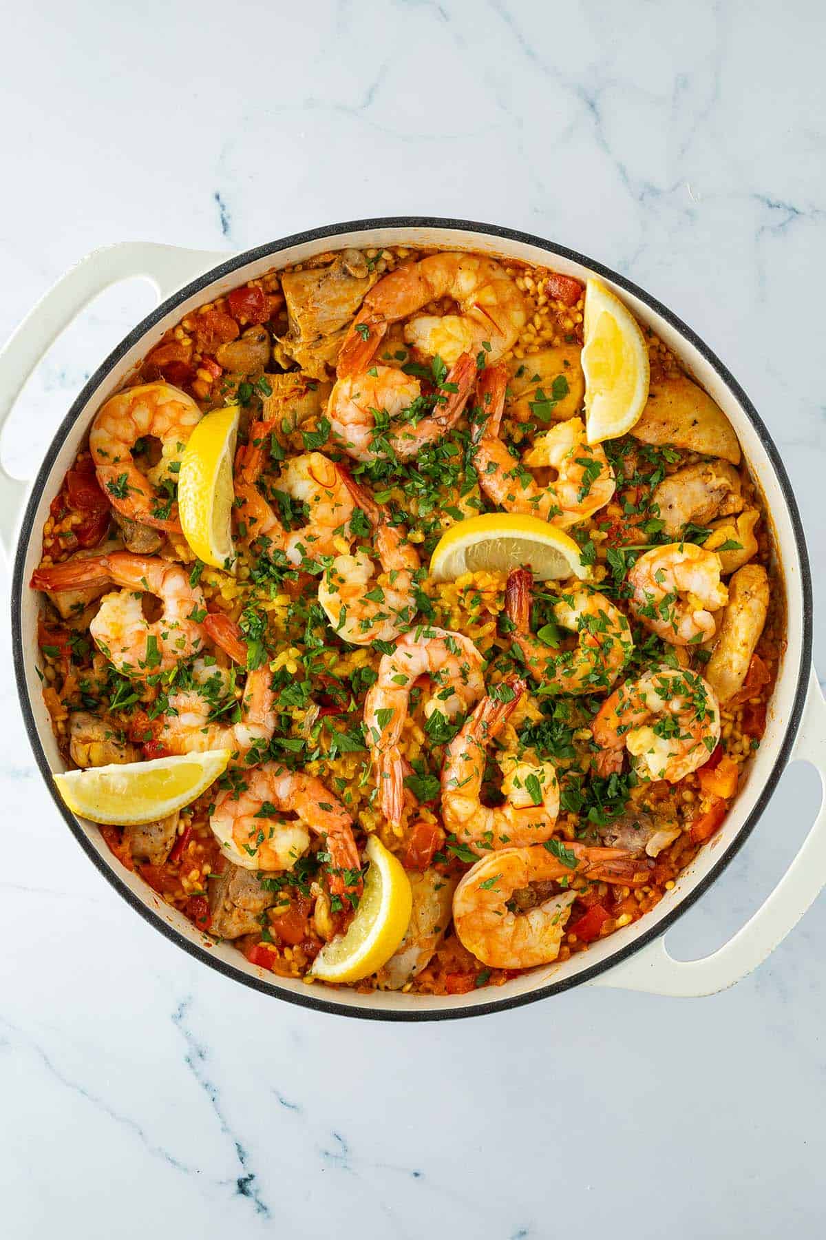 Fertige Paella mit H&auml;hnchen, Garnelen, Paprika und Safranreis, mit Petersilie und Zitronenspalten garniert.