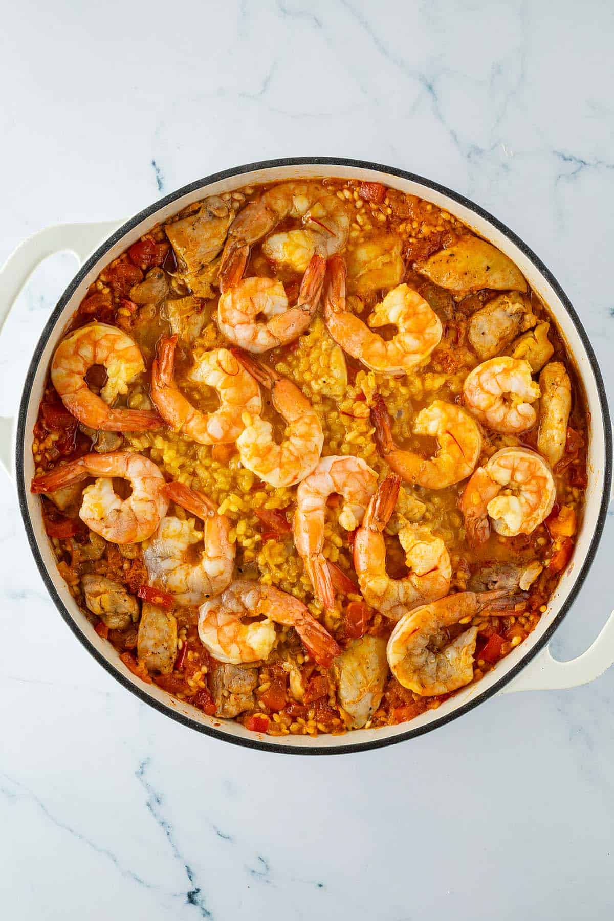 Paella mit Safranreis, H&auml;hnchen und Garnelen auf der Oberfl&auml;che w&auml;hrend des Garens in einer gro&szlig;en Pfanne.