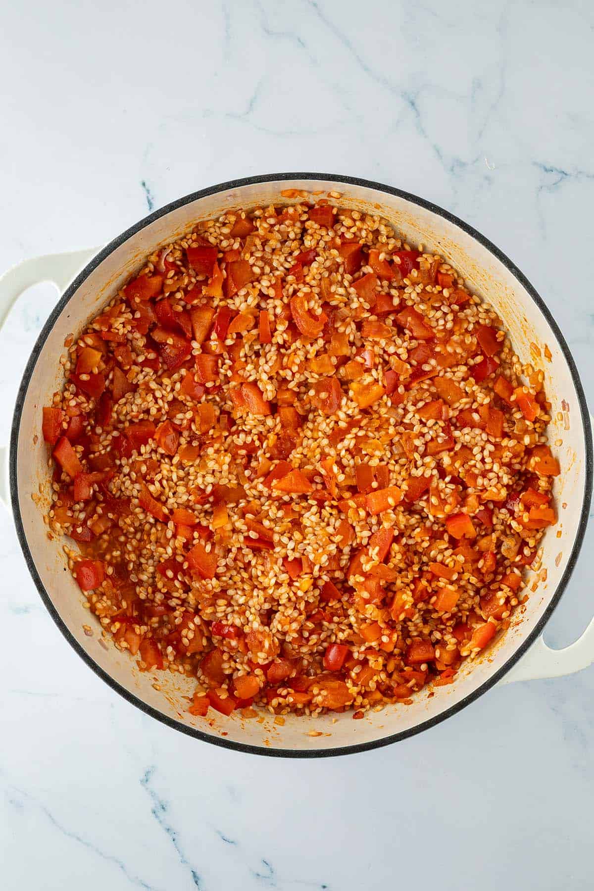 Paella-Reis mit gew&uuml;rfelter Paprika und Tomaten in einer gro&szlig;en Pfanne nach dem Abl&ouml;schen mit Wein.