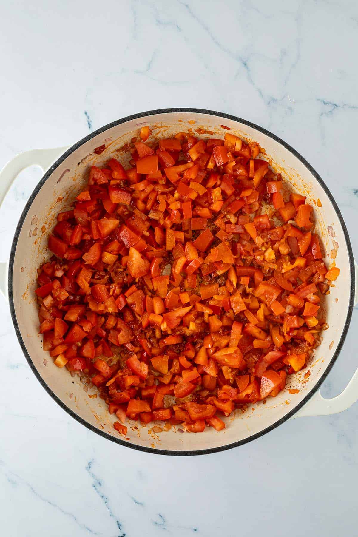 Angebratene Paprika, Tomaten und Zwiebeln als Gem&uuml;segrundlage f&uuml;r Paella in einer gro&szlig;en Pfanne.