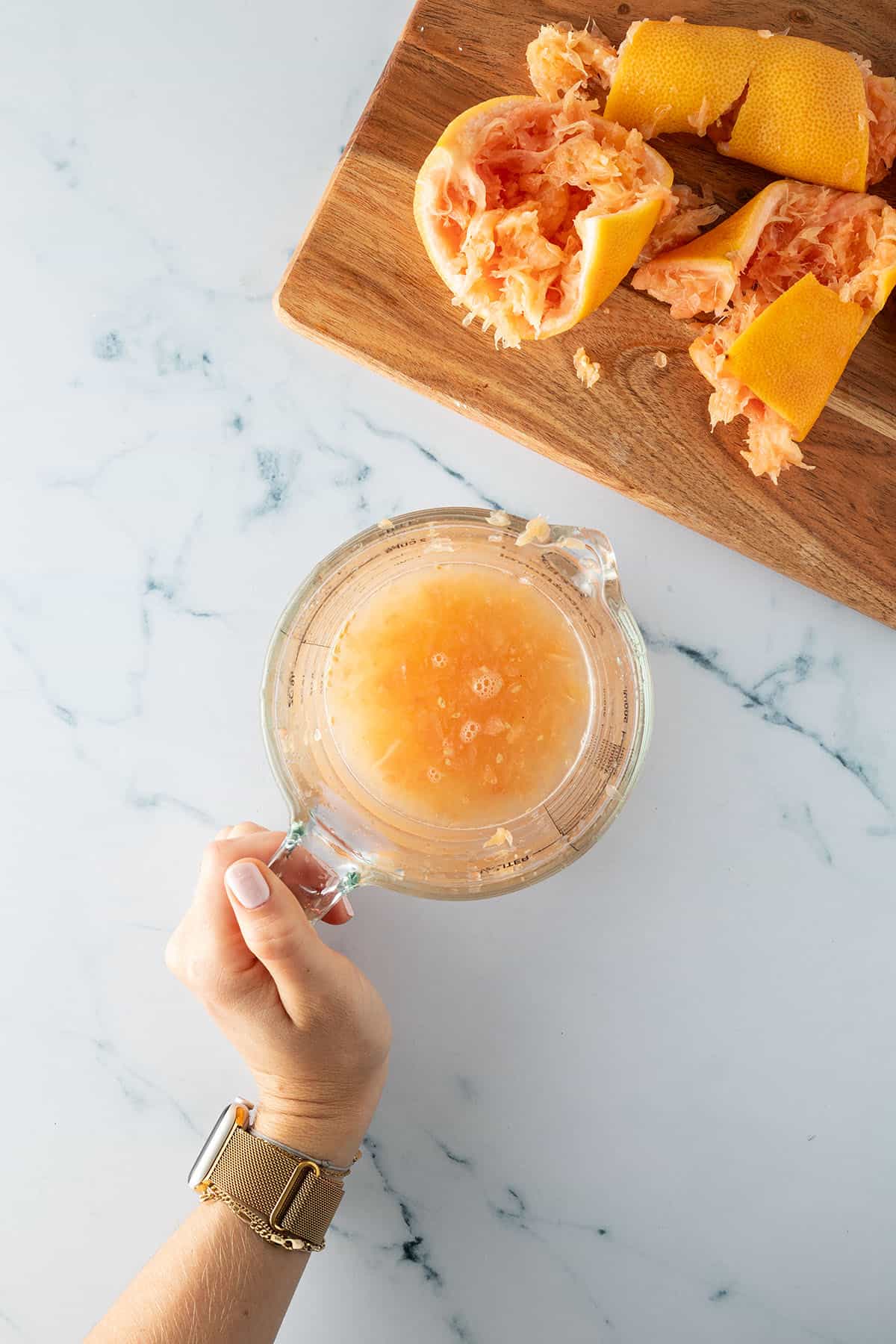 Ausgepresster Grapefruit Saft in einem Messbecher, daneben die ausgepressten Zitrusfr&uuml;chte.