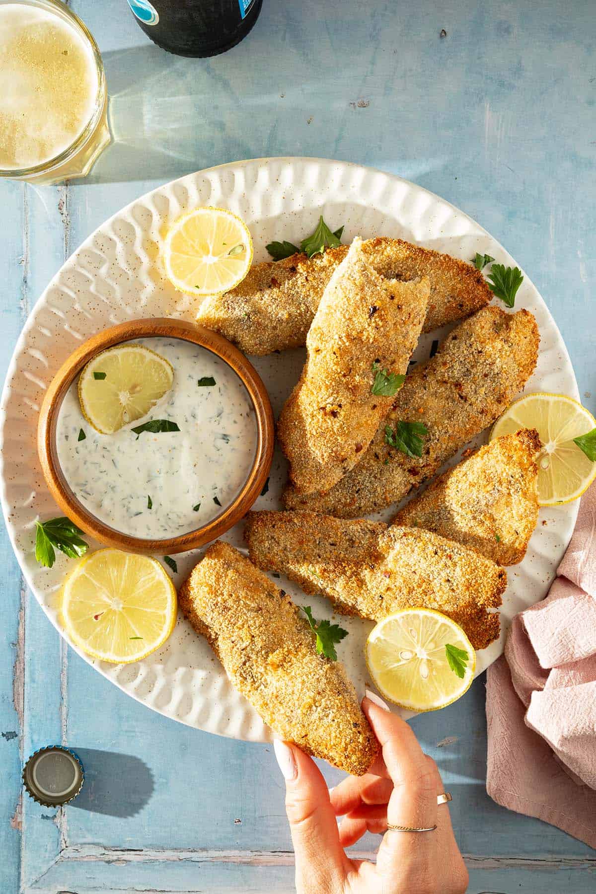 Teller mit mehreren panierten Fischfilets aus dem Airfryer, Zitronenscheiben und Kr&auml;uter-Dip, von oben fotografiert.