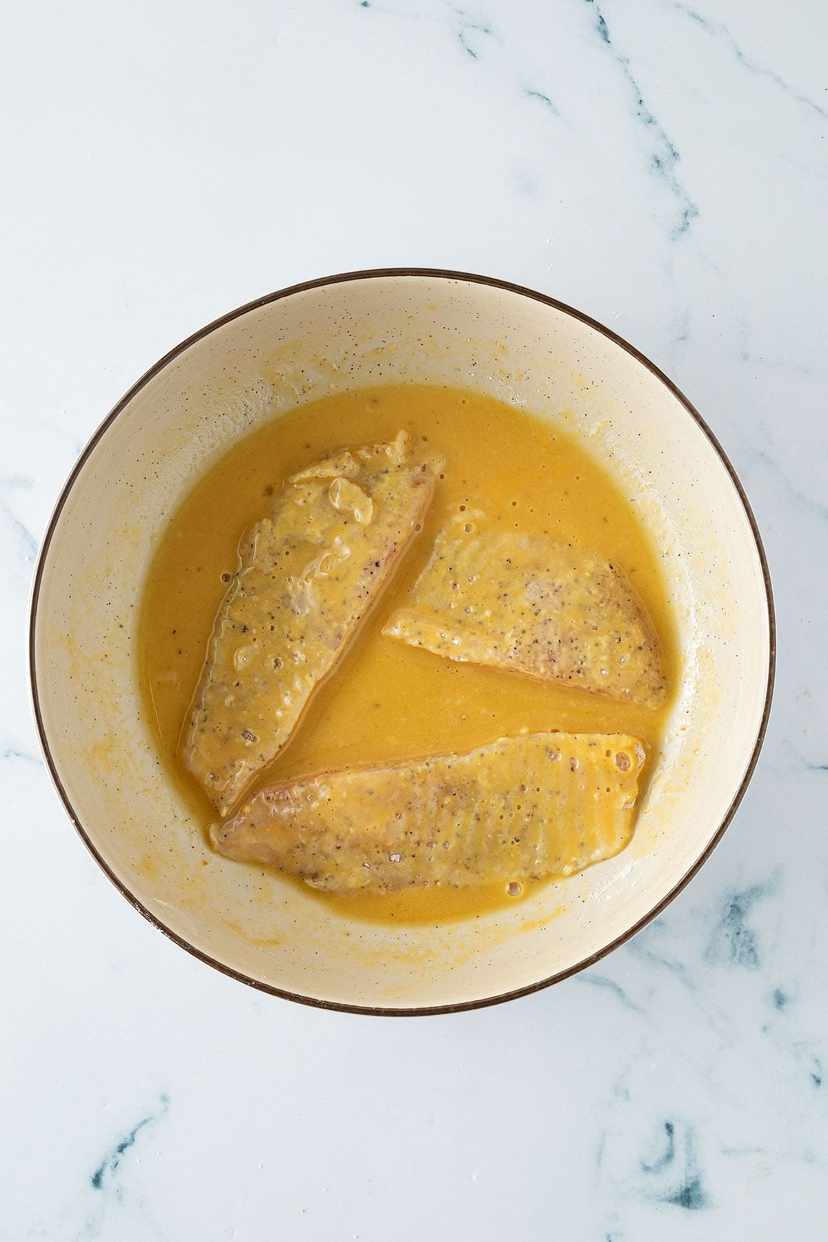 Fischfilets liegen in einer Sch&uuml;ssel mit gew&uuml;rzter Eimischung zum Panieren.